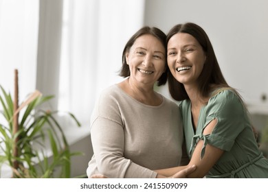 Cheerful elder mature mother and beautiful adult daughter woman hugging with heads touch, sitting close, looking away with toothy smiles, posing for shooting, enjoying family meeting - Powered by Shutterstock