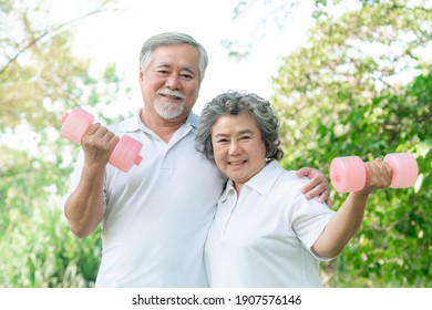 Cheerful Elderly Asian Man And Senior Asian Woman With Dumbbell For Workout In Park, They Smiling With Good Healthy Together