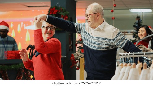 Cheerful elderly couple dancing in Christmas decorated clothing store, feeling xmas holiday mood spirit while browsing for presents. Senior customer being spinned by husband in fashion boutique - Powered by Shutterstock