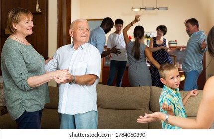 Cheerful Elderly Couple Dancing During Family Holiday Celebration Together With Their Children And Grandkids At Home