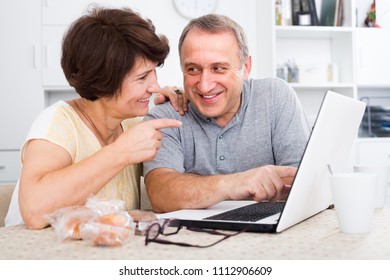 Cheerful Elderly Couple Looking On Laptop Screen  Indoors At Home Together.  Focus On Man
