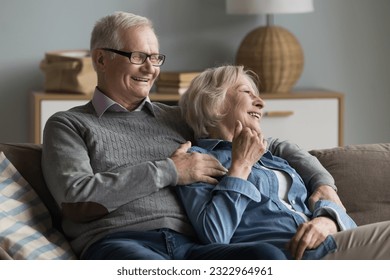 Cheerful elderly couple relaxing on couch in living room, laughing, enjoy conversation on carefree retired life. Lifelong happy marriage, harmonic relationships between mature spouses, eternal love - Powered by Shutterstock