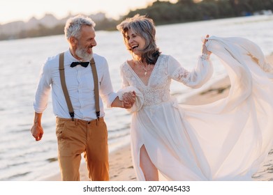 Cheerful elderly couple runs along beach holding hands. - Powered by Shutterstock