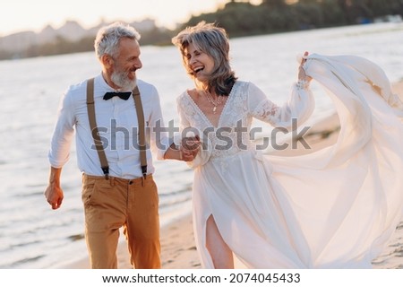 Cheerful elderly couple runs along beach holding hands.