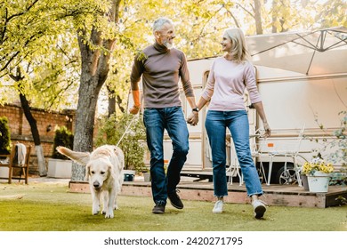 Cheerful elderly couple walking their dog in autumn garden. Mature spouses husband and wife spending time together with domestic animal golden retriever pet - Powered by Shutterstock