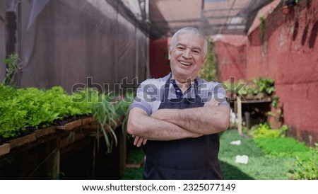 Cheerful Elderly Florist in Greenhouse, Delighted Plant Shop Proprietor Enjoying His Work with arms crossed. Portrait face close-up of older man working with Plants