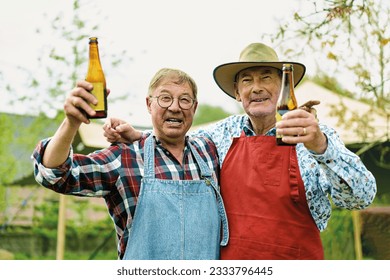 Cheerful Elderly Friends Toasting at Country Barbecue - Two happy elderly men, donning patterned shirts and barbecue aprons, toast with beer bottles in a country garden. - Powered by Shutterstock