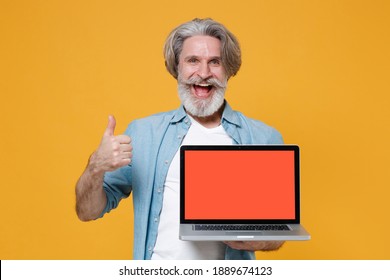 Cheerful Elderly Gray-haired Mustache Bearded Man In Casual Blue Shirt Posing Isolated On Yellow Background. People Lifestyle Concept. Hold Laptop Computer With Blank Empty Screen, Showing Thumb Up