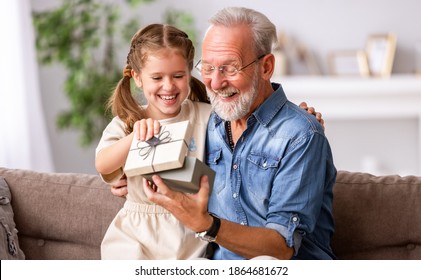 Cheerful elderly male smiling and gesticulating while receiving surprise gift from granddaughter during holiday celebration at home