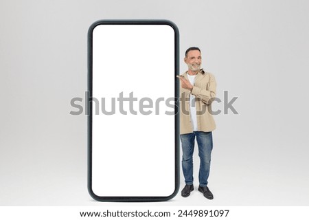 Cheerful elderly man gestures towards a blank large smartphone screen, isolated on white background, mockup, copy space