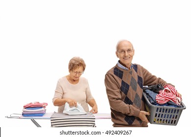 Cheerful Elderly Man Holding A Laundry Basket And A Mature Woman Ironing Isolated On White Background