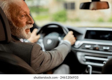 Cheerful elderly man in a suit driving leisurely, basking in the warm glow of a bright day - Powered by Shutterstock