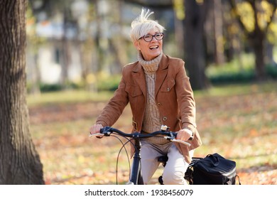 Cheerful Elderly Woman Riding Bicycle In Public Park. Activities For Older People