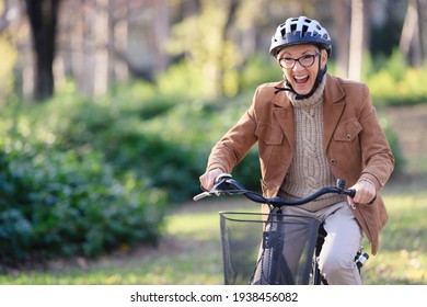 Cheerful Elderly Woman Riding Bicycle In Public Park. Activities For Older People