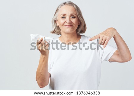 Cheerful elderly woman in a white T-shirt holding glasses in the hands of eye problems