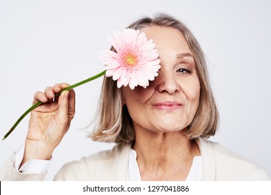 Cheerful elegant elderly woman holding a flower near the face on a gray background - Shutterstock ID 1297041886