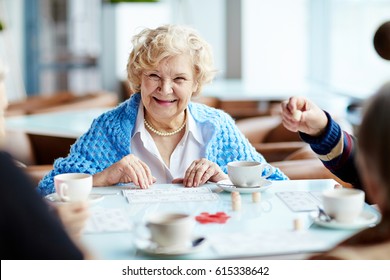 Cheerful Elegant-looking Elderly Woman Gathered With Her Friends In Lovely Coffeehouse And Playing Lotto Enthusiastically