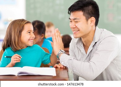 cheerful elementary school teacher and student high five in classroom