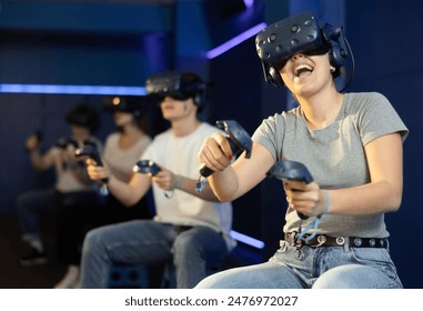 Cheerful emotional young woman in VR headset fully immersed in game, actively engaged in virtual reality world, manipulating objects or shooting targets with joysticks in hands.. - Powered by Shutterstock