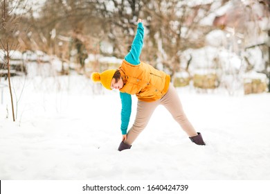 Cheerful Energetic Chubby Kid Girl In Yellow Hat And Warm Vest Is Engaged In Exercises, Stretching Outside In Winter. Concept Winter Sports Warm-up And Exercise, Sport At Any Time Of The Year