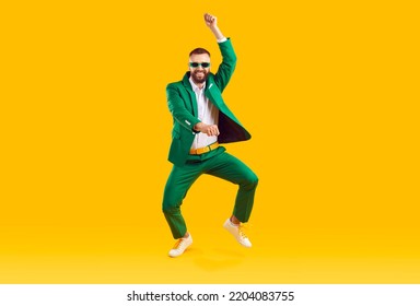 Cheerful energetic man has fun dancing in gangnam style at St. Patrick's Day party. Full length of man in trendy green suit and sunglasses of same color doing funny dance moves on orange background. - Shutterstock ID 2204083755