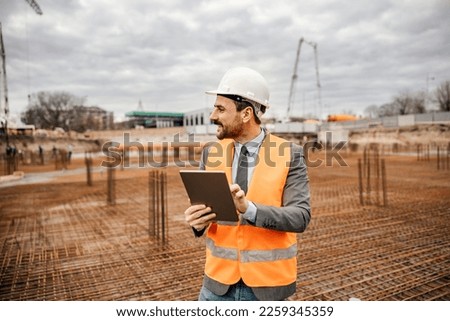 A cheerful engineer is holing tablet and checking works on tablet while standing ar reconstruction area.