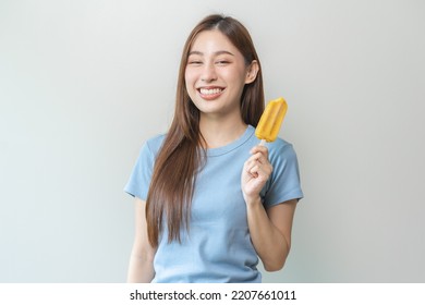 Cheerful Enjoy, Happy Cute Asian Woman Wearing Casual With Brunette Hair, Eating Popsicle, Teenage Girl Holding Ice Pop, Lolly Frozen Stick With Mango Yellow, Passion Fruit Ice Cream Tasty In Summer.