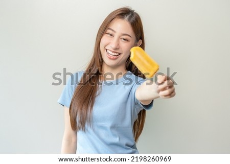 Cheerful enjoy, happy cute asian woman wearing casual with brunette hair, eating popsicle, teenage girl holding ice pop, lolly frozen stick with mango yellow, passion fruit ice cream tasty in summer.