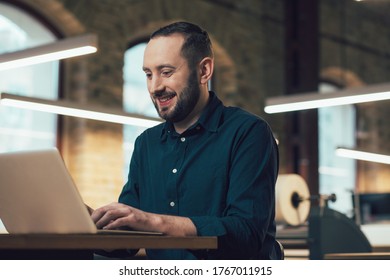 Cheerful Enthusiastic Employee Sitting At The Table In Publishing House And Smiling While Using A Modern Laptop