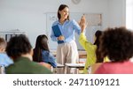 Cheerful European female teacher giving high five to pupil girl sitting at desk. Education, teaching, learning and school concept