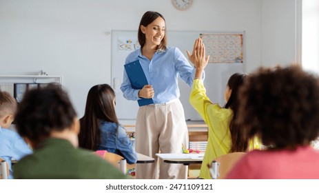 Cheerful European female teacher giving high five to pupil girl sitting at desk. Education, teaching, learning and school concept - Powered by Shutterstock