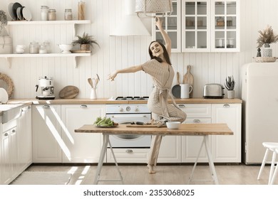 Cheerful excited active young woman having fun in home kitchen, dancing at table with organic food, fresh vegetables for salad, celebrating culinary success, feeling full of energy due to healthy diet - Powered by Shutterstock