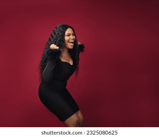 A cheerful excited African woman is excited to win raffle draw product empty copy space standing over isolated red background  Model young girl laughing promotion  Advertisement presenting once
