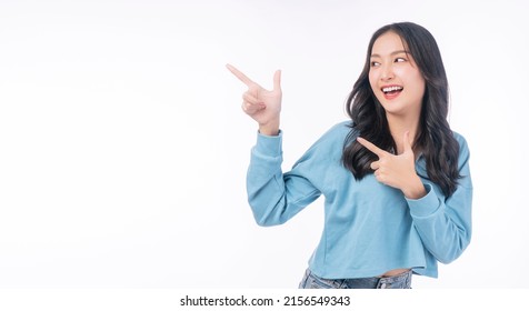Cheerful excited asian woman use finger pointing to side with product or empty copy space standing over isolated white background. Model young girl laughing promotion. Advertisement presenting concept - Shutterstock ID 2156549343