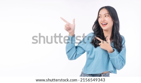 Cheerful excited asian woman use finger pointing to side with product or empty copy space standing over isolated white background. Model young girl laughing promotion. Advertisement presenting concept