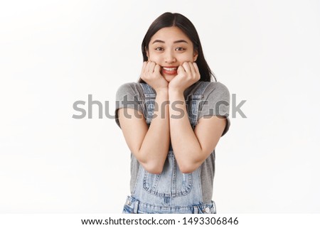 Cheerful excited cute happy asian brunette girl touch cheeks smiling enertained amused awaiting favorite singer come on stage standing joyfully cannot wait eager see performance white background
