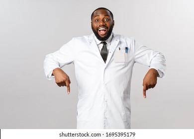 Cheerful Excited, Happy African-american Male Doctor Inviting See Great Thing, Pointing Fingers Down, Ask To Look And Check-out Awesome Product, Guarantee Best Quality, Grey Background