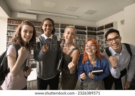 Cheerful excited high school mates celebrating educational achievement, successful teamwork, posing in campus college library, making winner fist gesture, looking at camera, smiling, shouting