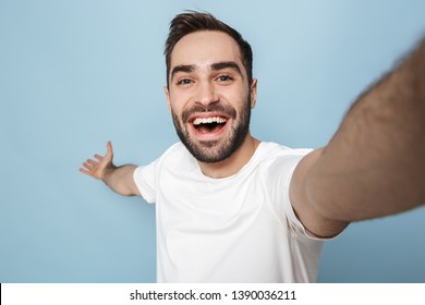 Cheerful Excited Man Wearing Blank T-shirt Standing Isolated Over Blue Background, Taking Selfie