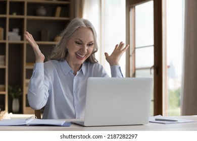 Cheerful excited mature business freelance woman receiving great good news, sitting at laptop at home, making winner yes hands, laughing, shouting for joy, euphoria, feeling overjoyed