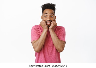 Cheerful And Excited Young African American Guy, Squeeze His Cheeks And Smiling From Anticipation And Excitement, Hear Amazing News, Waiting Hopeful, White Background