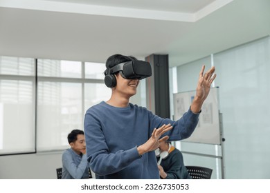 A cheerful and excited young Asian male developer tested a new VR game on a VR headset in the meeting with team. Virtual reality - Powered by Shutterstock