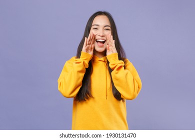 Cheerful excited young brunette asian woman 20s wearing basic yellow hoodie standing screaming with hands gesture near mouth looking camera isolated on pastel violet colour background studio portrait - Powered by Shutterstock