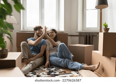 Cheerful excited young couple planning renovation after moving into new apartment, choosing interior material samples of tile, laughing, giving high five, clapping hands at cardboard boxes - Powered by Shutterstock