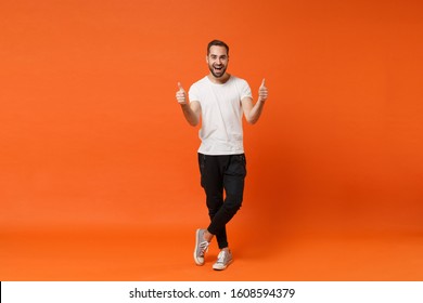 Cheerful Excited Young Man In Casual White T-shirt Posing Isolated On Bright Orange Wall Background Studio Portrait. People Sincere Emotions Lifestyle Concept. Mock Up Copy Space. Showing Thumbs Up