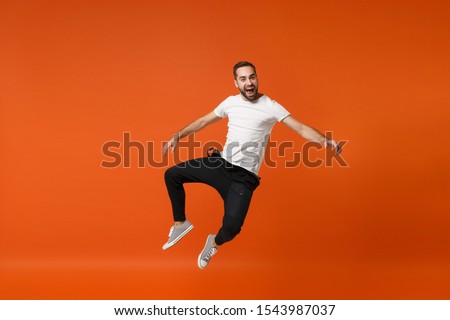 Cheerful excited young man in casual white t-shirt posing isolated on bright orange wall background studio portrait. People lifestyle concept. Mock up copy space. Having fun, fooling around, jumping