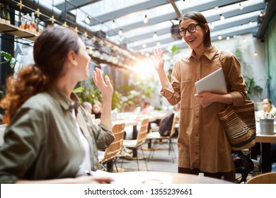 Cheerful Excited Young Women Waving Hands While Greeting Each Other In Cafe, They Meeting By Chance In Public Place