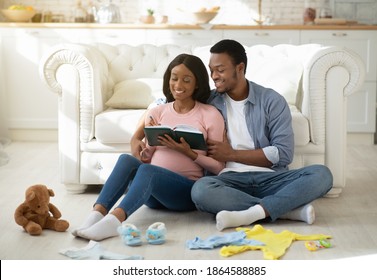 Cheerful Expectant Couple Writing List Of Baby Stuff For Maternity Hospital In Living Room. Happy Future Mom And Dad Preparing Things For Birthing Center, Making Notes In Copybook