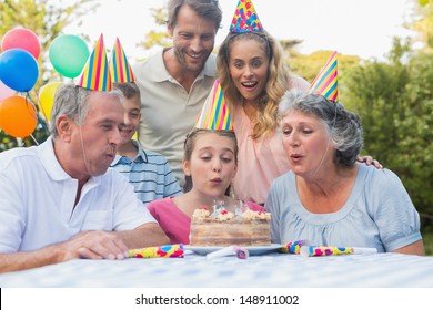 Cheerful Extended Family Watching Girl Blowing Out Birthday Candles Outside At Picnic Table