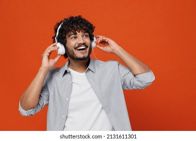 Cheerful Exultant Happy Young Bearded Indian Man 20s Years Old Wears Blue Shirt Listen Music In Headphones Dance Have Fun Gesticulating Hands Relax Isolated On Plain Orange Background Studio Portrait